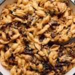 Creamy Cajun Chicken Pasta with sun-dried tomatoes and fresh herbs in a white skillet on a rustic grey wooden surface. Perfect comfort food recipe for dinner or special occasions.