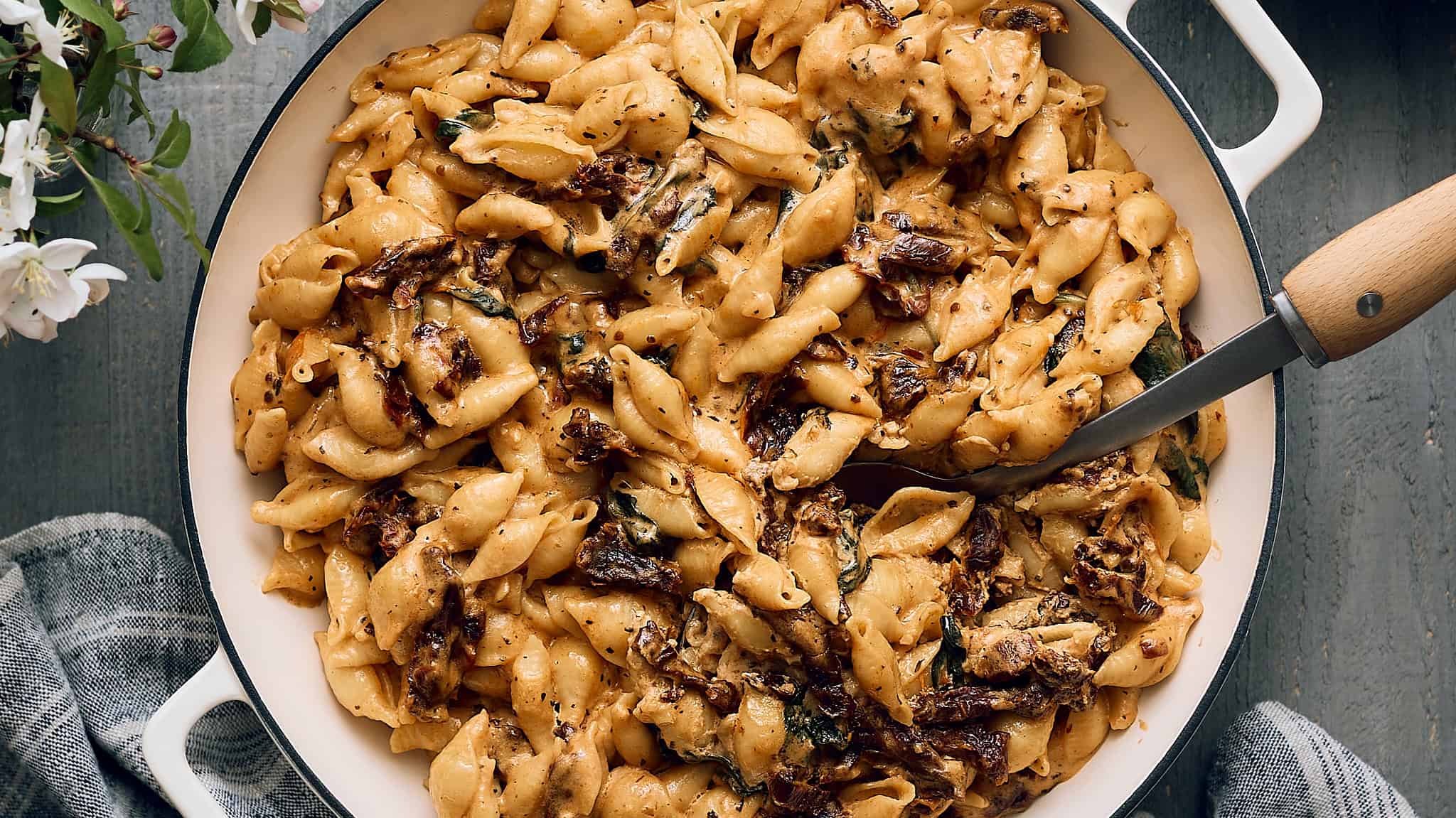 Creamy Cajun Chicken Pasta with sun-dried tomatoes and fresh herbs in a white skillet on a rustic grey wooden surface. Perfect comfort food recipe for dinner or special occasions.
