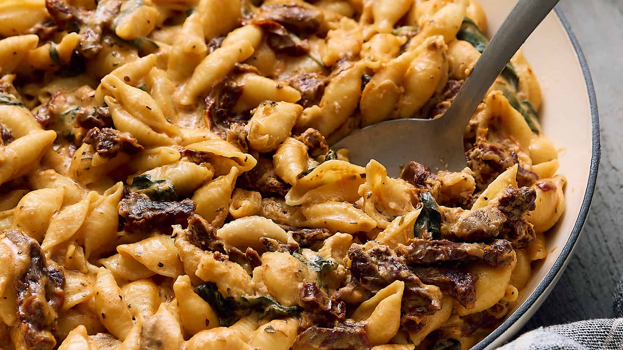 Creamy beef and spinach tortellini casserole in a white baking dish with a metal spoon for serving. Perfect comfort food recipe featuring cheese-filled pasta, tender beef, spinach, and creamy sauce.
