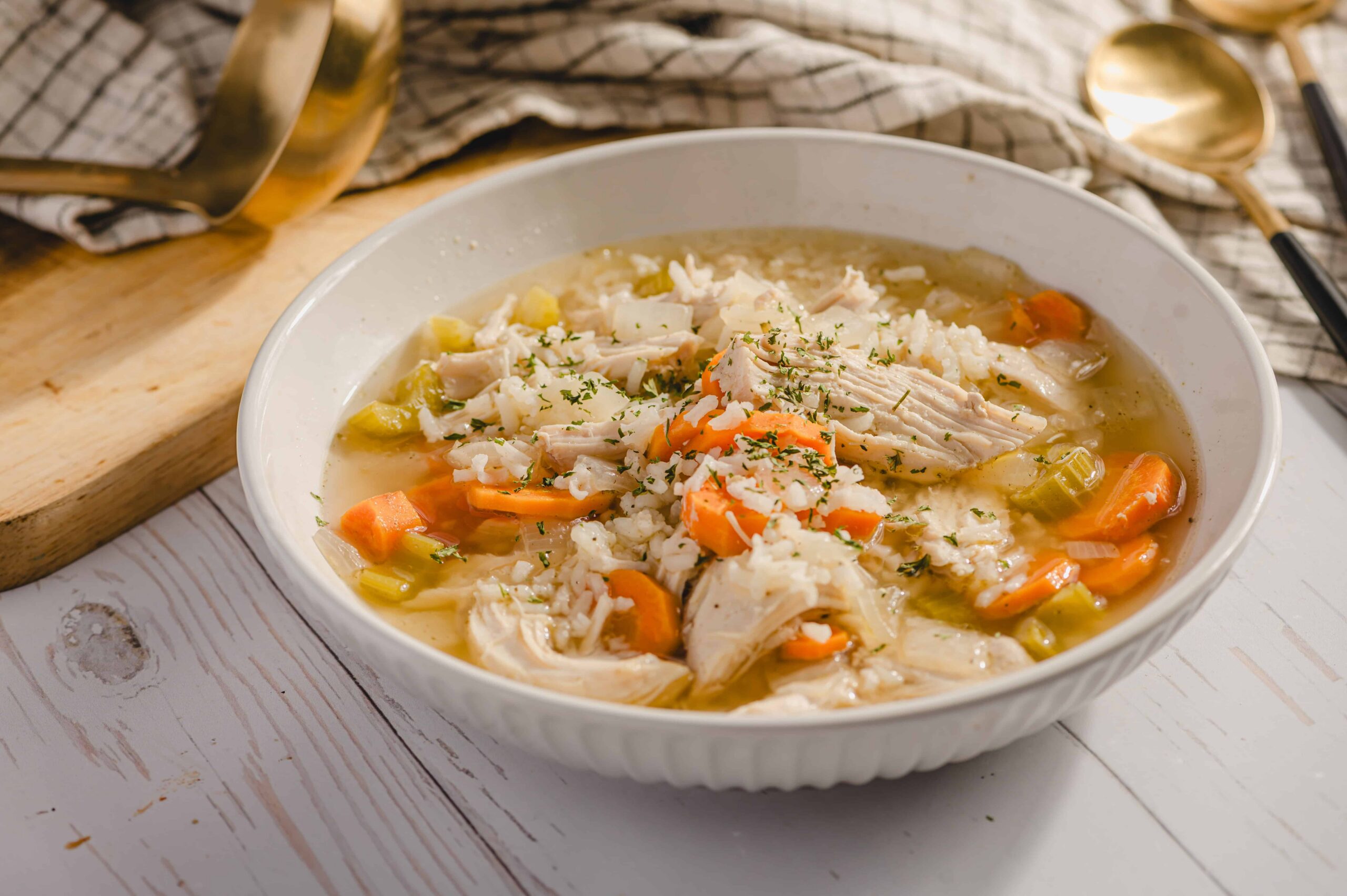 Comforting chicken and vegetable soup in a white bowl, featuring shredded chicken, carrots, celery, and herbs, served on a rustic wooden table.