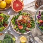 Fresh vegetable salads with broccoli, red cabbage, lettuce, and tomato, served with lemon wedges and topped with seeds and grains, perfect for a healthy meal.