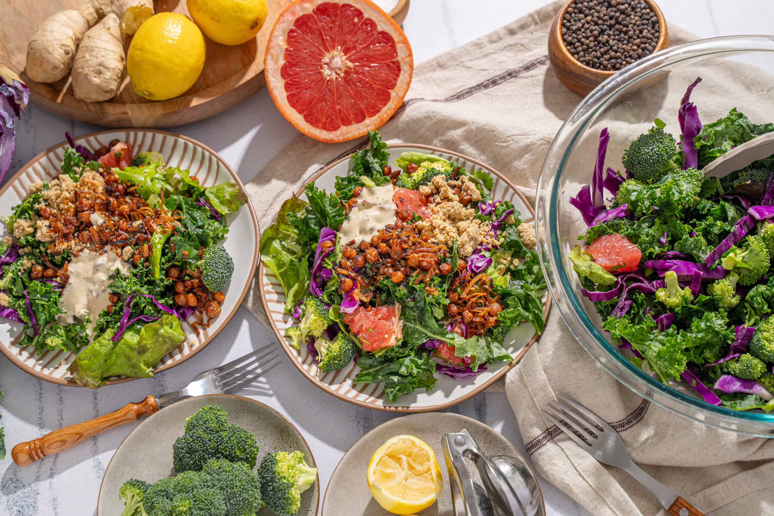 Fresh vegetable salads with broccoli, red cabbage, lettuce, and tomato, served with lemon wedges and topped with seeds and grains, perfect for a healthy meal.