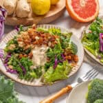Fresh vegetable salad with broccoli, cabbage, cherry tomatoes, and a creamy dressing, served on decorative plates, with fresh ingredients like grapefruit, ginger, and garlic surrounding it.