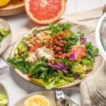 Fresh mixed salad with greens, roasted chickpeas, smoked salmon, cabbage, and creamy dressing on a white plate.
