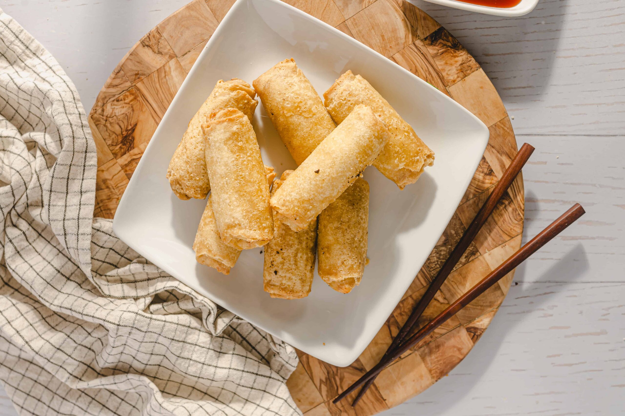 Crispy spring rolls on a white plate with chopsticks, served on a wooden platter, perfect for appetizer or snack, featured on Hey Recipe website.