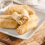 Golden crispy egg rolls filled with shrimp, vegetables, and meat, served on a white plate, perfect as an appetizer or snack, on a rustic wooden board.