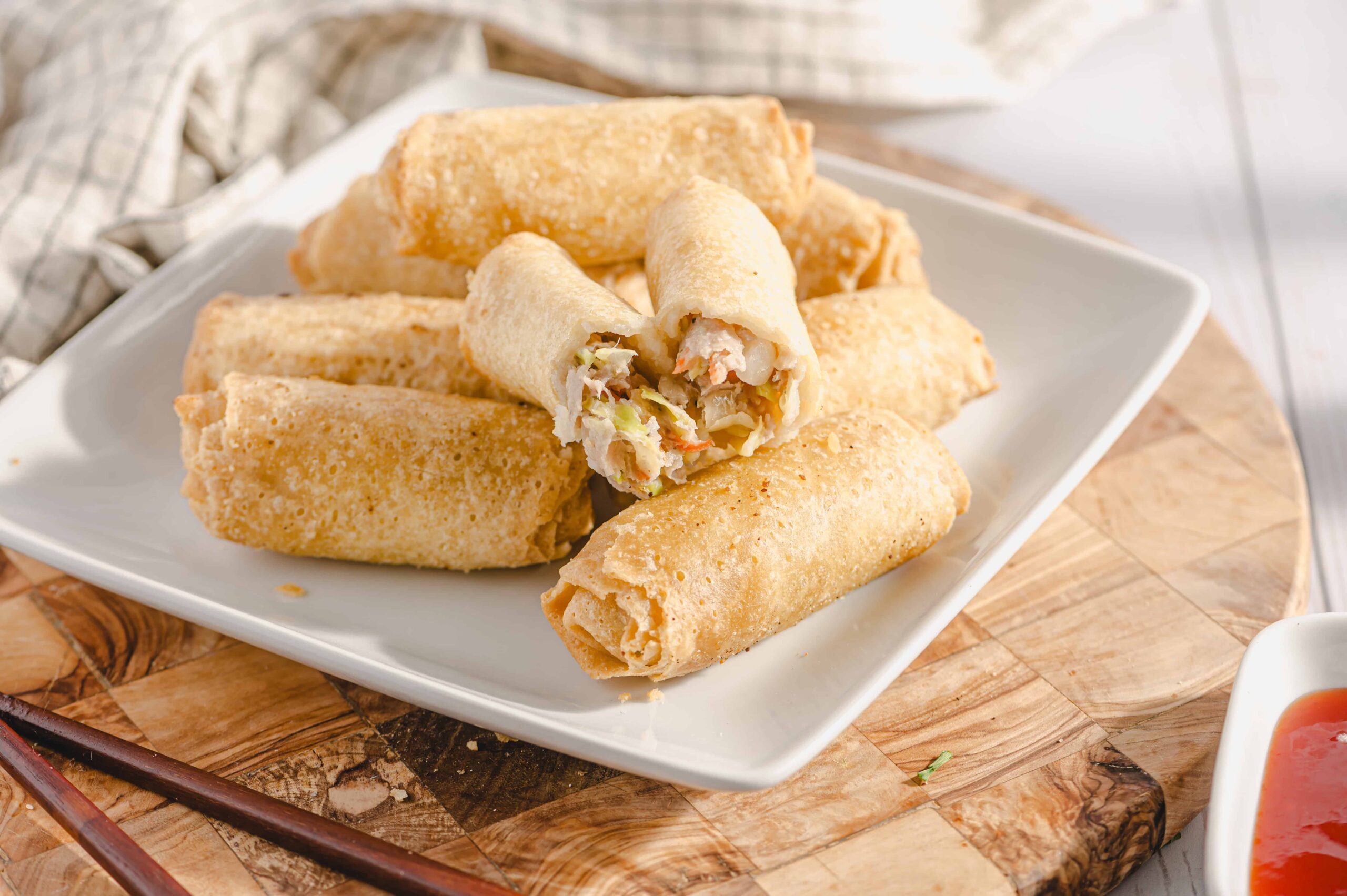 Golden crispy egg rolls filled with shrimp, vegetables, and meat, served on a white plate, perfect as an appetizer or snack, on a rustic wooden board.