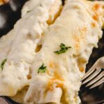 Creamy cheesy baked enchiladas with melted cheese and fresh cilantro in a black serving dish.