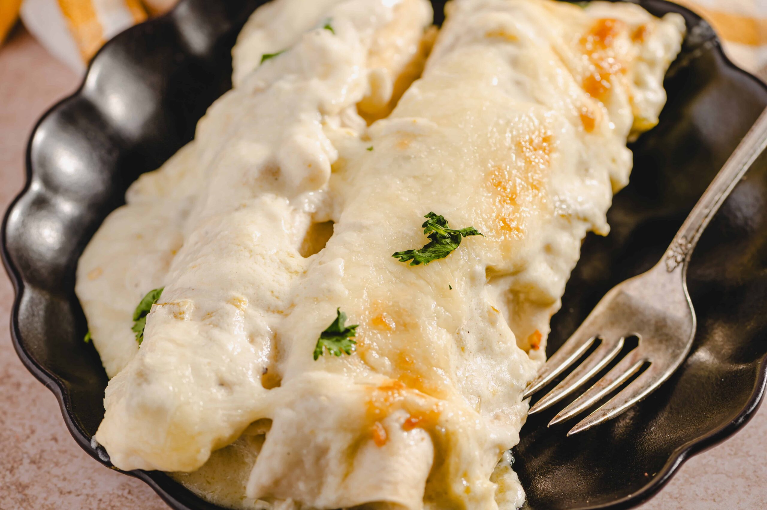 Creamy cheesy baked enchiladas with melted cheese and fresh cilantro in a black serving dish.