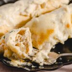 Creamy chicken and cheese enchiladas in a black serving dish, topped with melted cheese; close-up of a cheesy baked Mexican casserole dish, comfort food, and savory dinner idea.