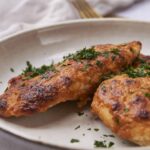 Baked chicken and potato steaks garnished with chopped parsley on a light ceramic plate for a healthy homemade dinner.