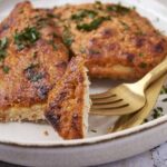 Juicy baked chicken breasts topped with herbs on a white plate.