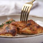 Crispy baked chicken thighs garnished with herbs on a white plate.