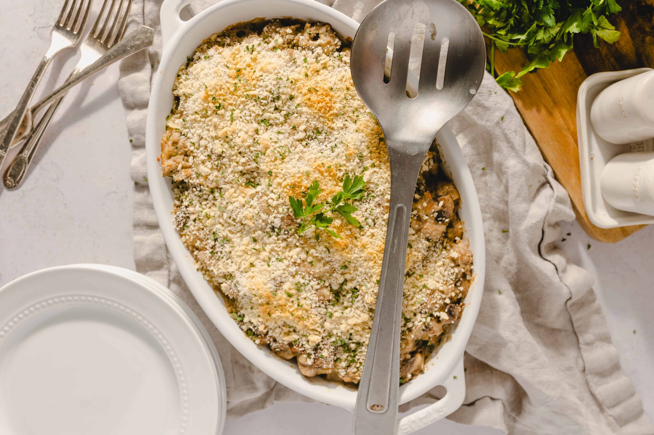 Creamy cheesy baked eggplant casserole garnished with fresh parsley in a white oval dish.