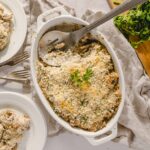 Creamy chicken casserole with breadcrumbs and herbs, served in a white dish with fresh parsley garnish, accompanied by plates of chicken, perfect for comfort food recipes.