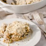 Creamy chicken and mushroom casserole topped with grated cheese and herbs on a white plate, served with silver forks and a side dish in the background, perfect comfort food.