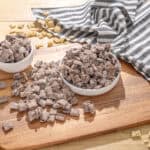 Colorful frozen snack cubes with raisins, chocolate chips, and biscuit pieces in bowls on a wooden cutting board. Perfect for quick and tasty treats or dessert toppings, ideal for quick snacks or creative dessert ideas.