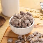 Sweet chocolate-covered cereal squares in a white bowl with scattered cereal pieces and a glass of milk on a wooden table. Perfect for breakfast or snacks.