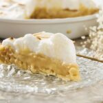 Buttermilk pie with a golden crust and creamy filling, topped with whipped meringue, served on a clear glass plate, perfect for dessert.