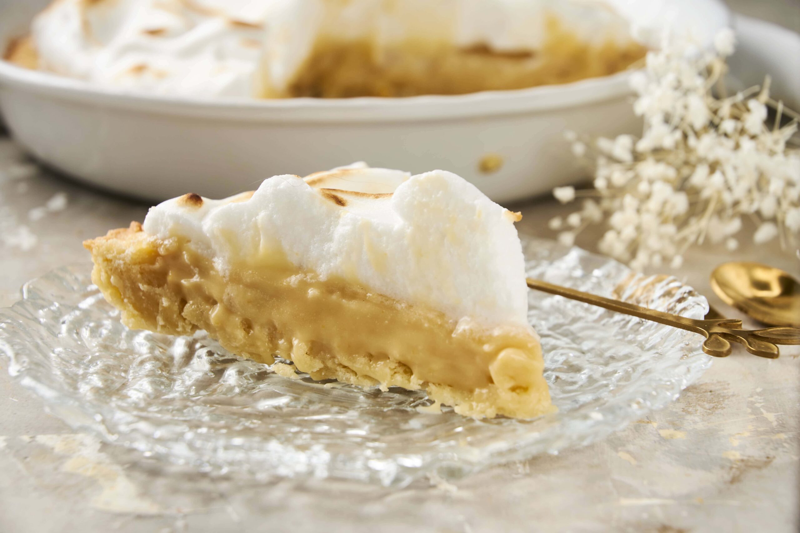 Buttermilk pie with a golden crust and creamy filling, topped with whipped meringue, served on a clear glass plate, perfect for dessert.