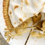 Creamy lemon meringue pie with golden toasted peaks on a white serving dish, with a slice removed revealing lemon filling and meringue topping. Perfect for dessert lovers and baking enthusiasts.