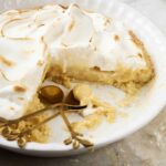 Golden baked lemon meringue pie with toasted peaks, creamy lemon filling, and flaky crust served on a white plate. Perfect for dessert, featuring meringue topping and lemon custard.