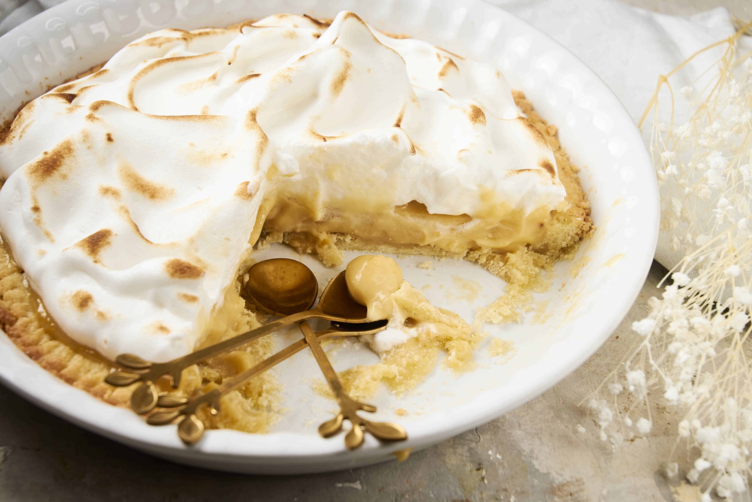 Golden baked lemon meringue pie with toasted peaks, creamy lemon filling, and flaky crust served on a white plate. Perfect for dessert, featuring meringue topping and lemon custard.