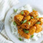 Crispy orange chicken served over steamed rice garnished with chopped green onions. A flavorful, easy-to-make Asian-inspired dish perfect for dinner or lunch.