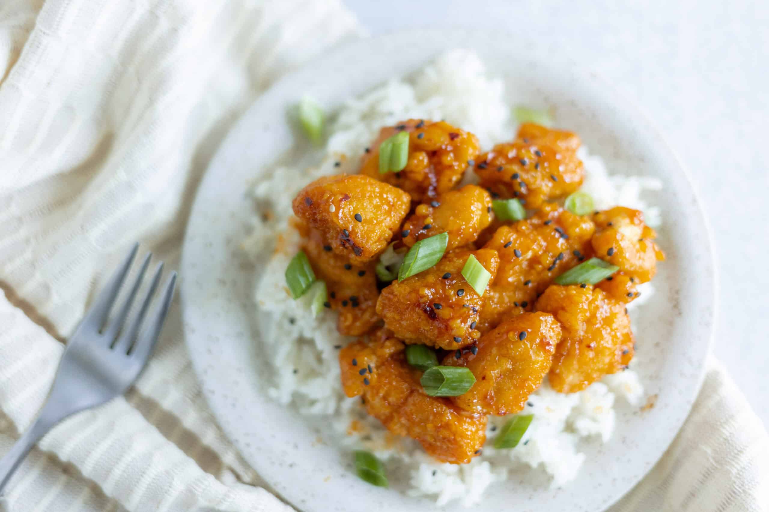 Crispy orange chicken served over steamed rice garnished with chopped green onions. A flavorful, easy-to-make Asian-inspired dish perfect for dinner or lunch.