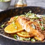 Sushi with fresh salmon, orange slices, green onions, sesame seeds, and sauce served in a rustic black bowl, highlighting healthy, flavorful seafood dishes.
