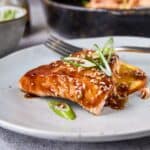 Succulent salmon fillet glazed with teriyaki sauce, garnished with sliced green onions and sesame seeds, served on a white plate for an easy, flavorful seafood recipe.