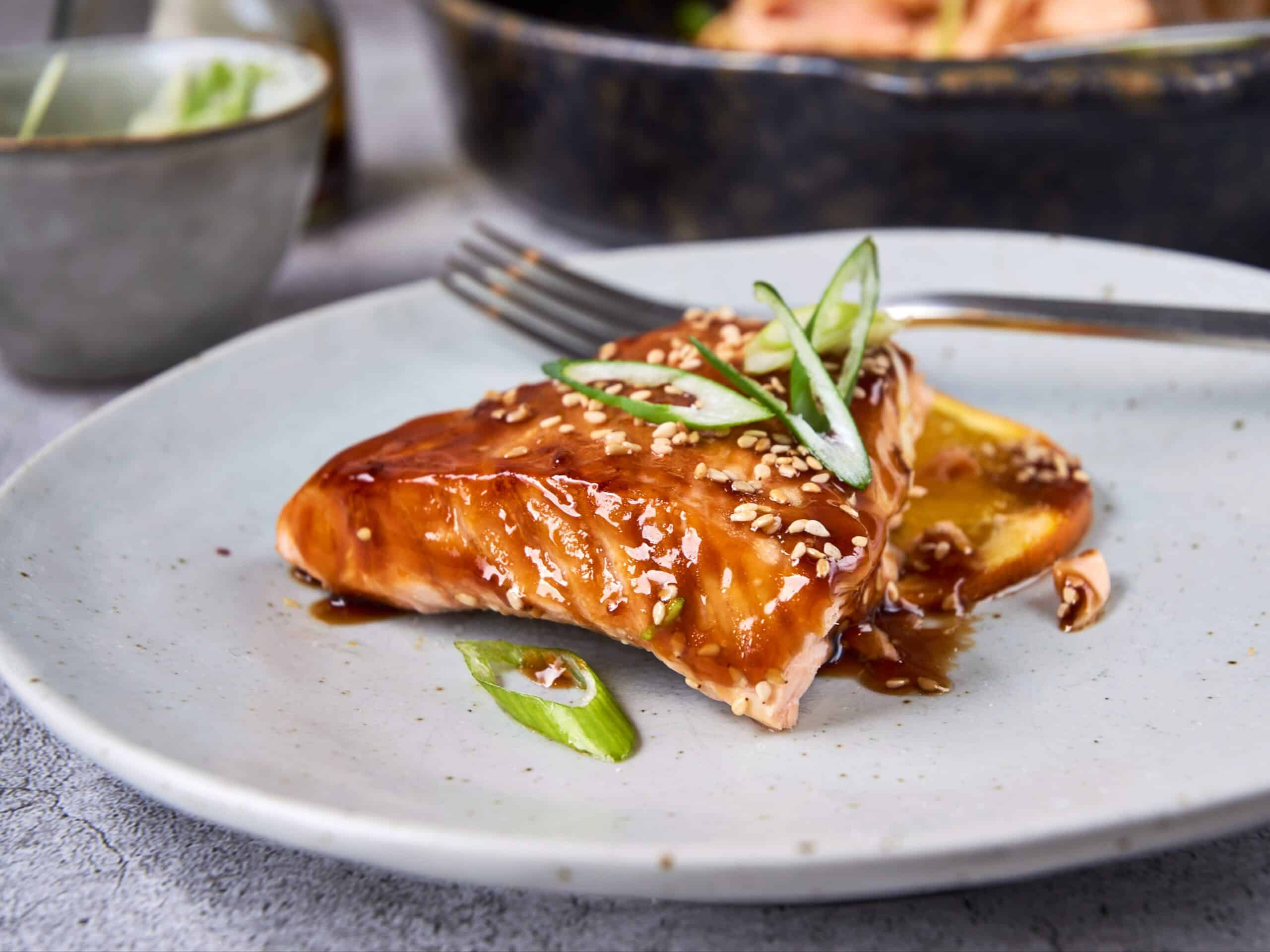Succulent salmon fillet glazed with teriyaki sauce, garnished with sliced green onions and sesame seeds, served on a white plate for an easy, flavorful seafood recipe.