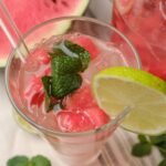Refreshing watermelon lemonade garnished with fresh mint and a lime wedge, served in a clear glass with ice cubes, perfect for summer drinks and fruity cocktail recipes.