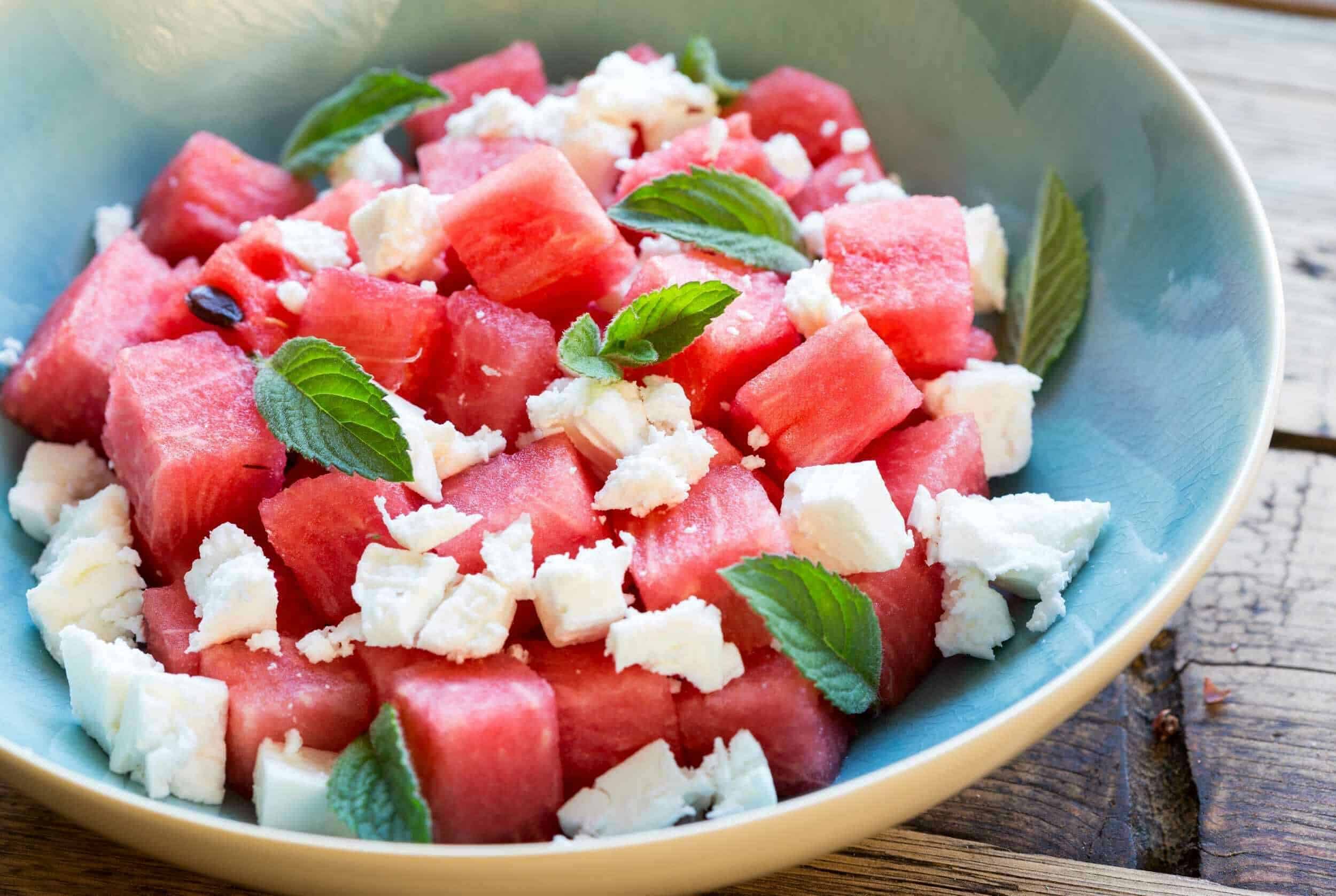 Juicy watermelon cubes with crumbled feta cheese, fresh mint leaves, and a rustic wooden background. A refreshing fruit salad perfect for summer.