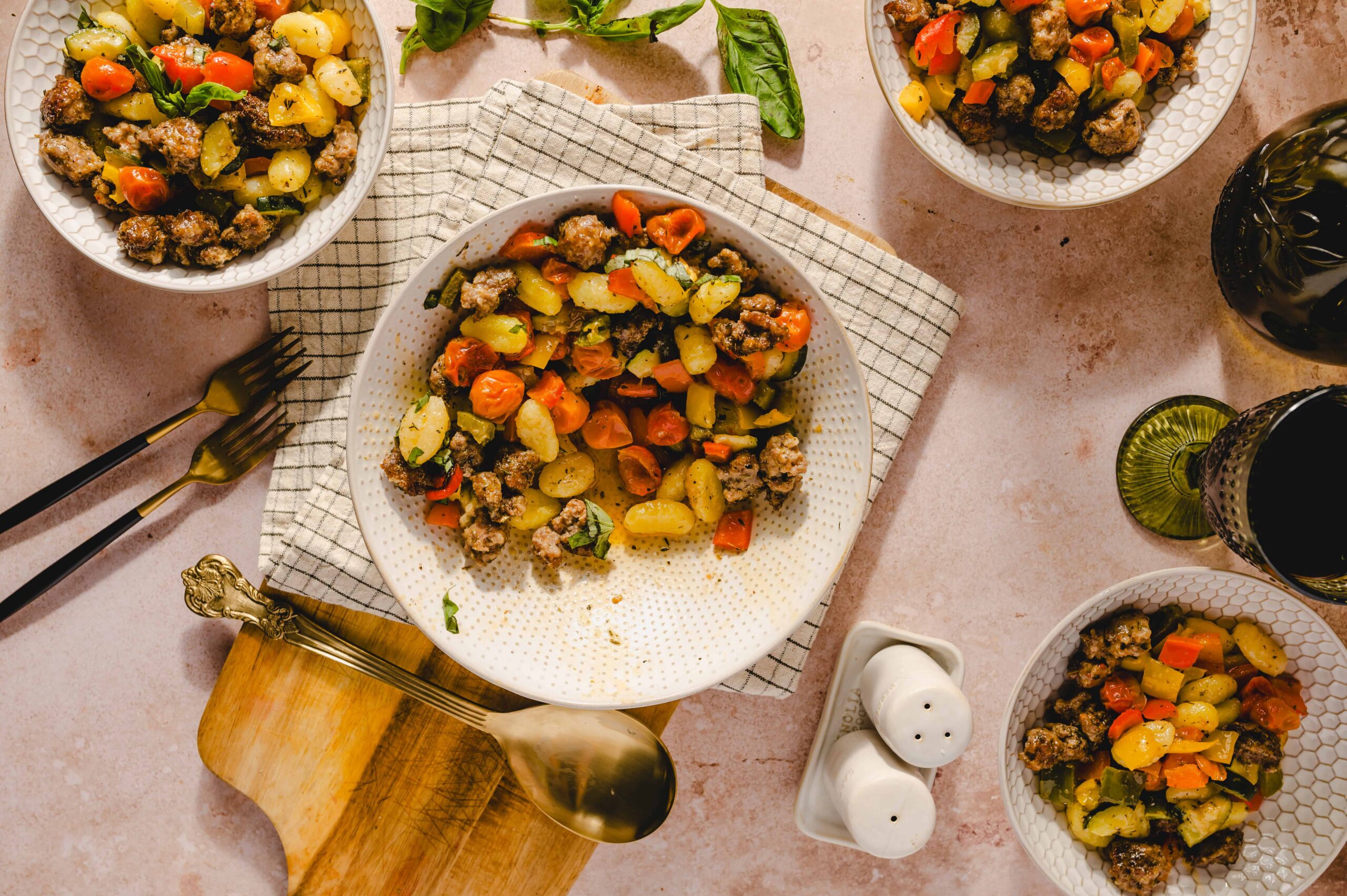 Thin colorful vegetable and minced beef salad served in white ceramic bowls on a pink countertop. Fresh herbs, vintage cutlery, and a glass of red wine add a charming rustic vibe.