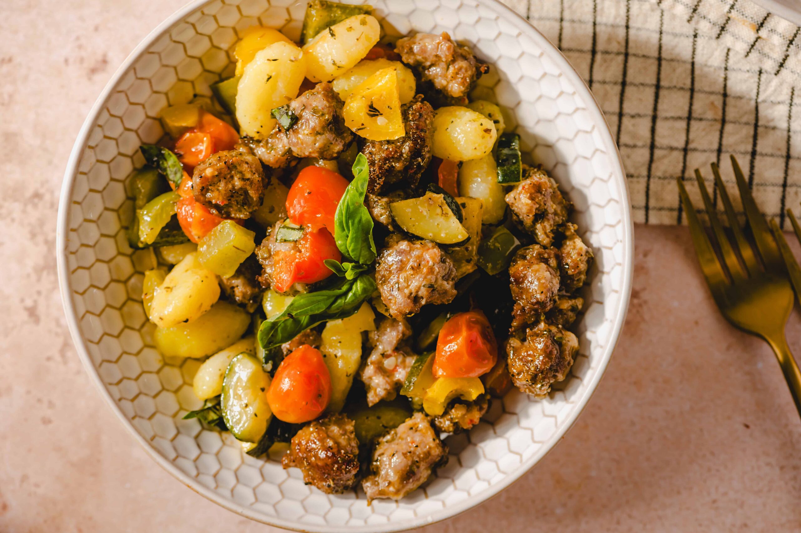 Juicy meatball and vegetable salad with potatoes, cherry tomatoes, zucchini, and fresh basil in a white honeycomb bowl, perfect for a healthy and flavorful meal.