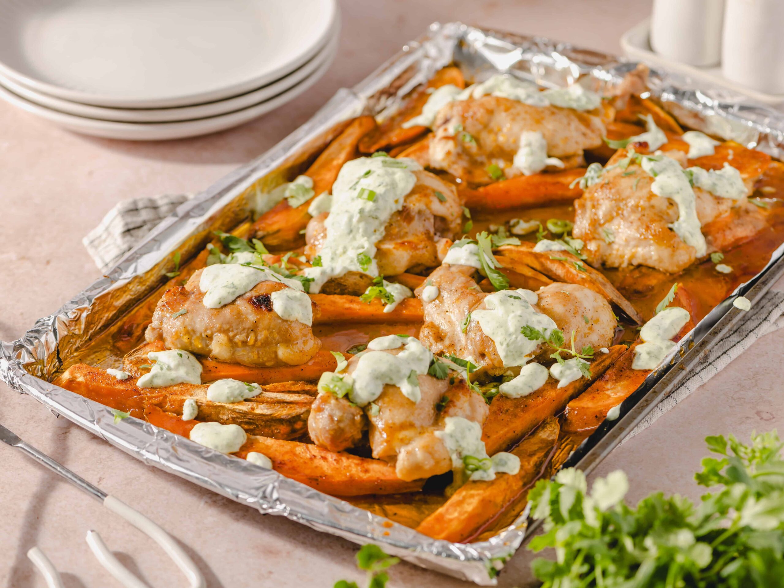 Roasted chicken with sweet potatoes and green sauce, served on a baking sheet covered with aluminum foil, garnished with fresh herbs. Perfect for easy, healthy meals and meal prep.