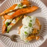 Roasted sweet potato wedges with cilantro lime sauce served alongside baked chicken topped with creamy herb dressing on a white plate.