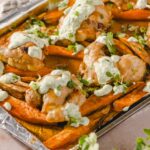 Roasted sweet potatoes with chicken, topped with cilantro and a creamy, herb-infused sauce, served on a baking sheet with aluminum foil for a delicious and healthy meal.