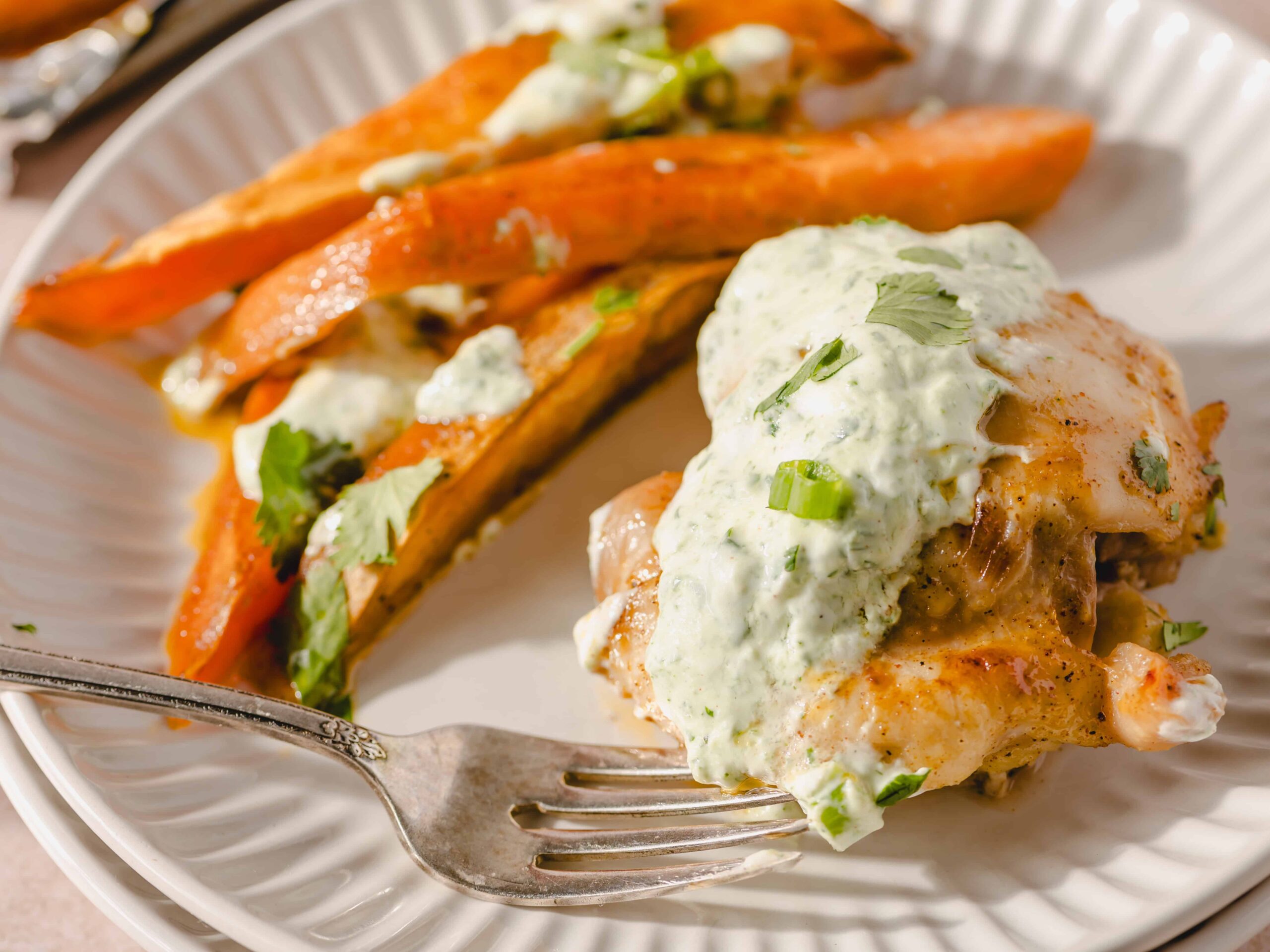 Golden-brown baked sweet potatoes topped with creamy herb sauce, served with fresh cilantro and green onions, on a white plate. Perfect for healthy, flavorful sweet potato recipes.