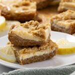 Sweet lemon bars with crumbly crust and creamy filling, garnished with fresh lemon slices on a white plate, perfect for dessert or afternoon snack.