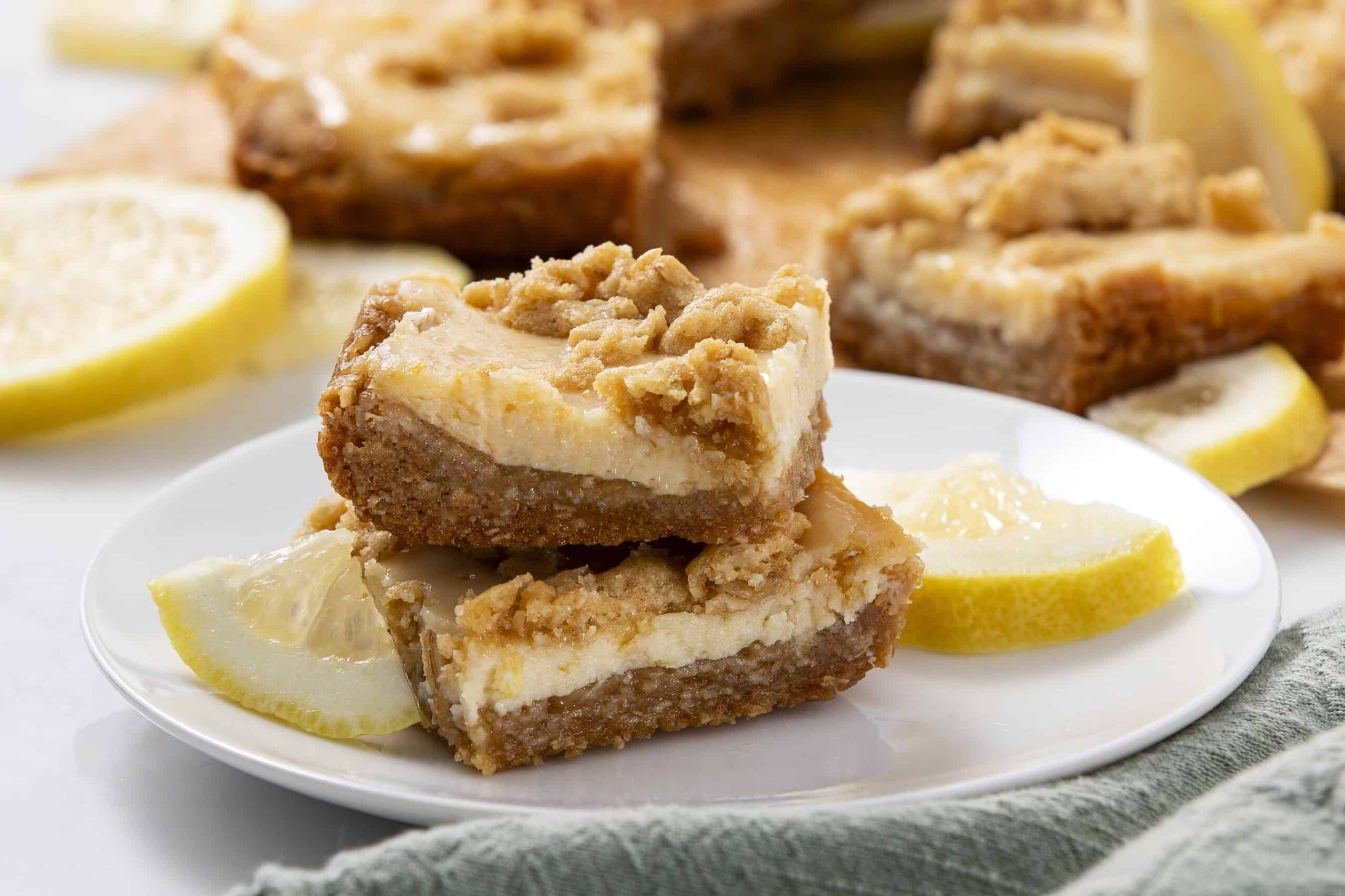 Sweet lemon bars with crumbly crust and creamy filling, garnished with fresh lemon slices on a white plate, perfect for dessert or afternoon snack.