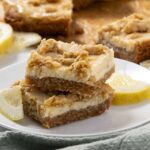 Delicious lemon dessert bars with a crumbly topping and creamy filling on a white plate, garnished with fresh lemon slices, perfect for spring or summer desserts.