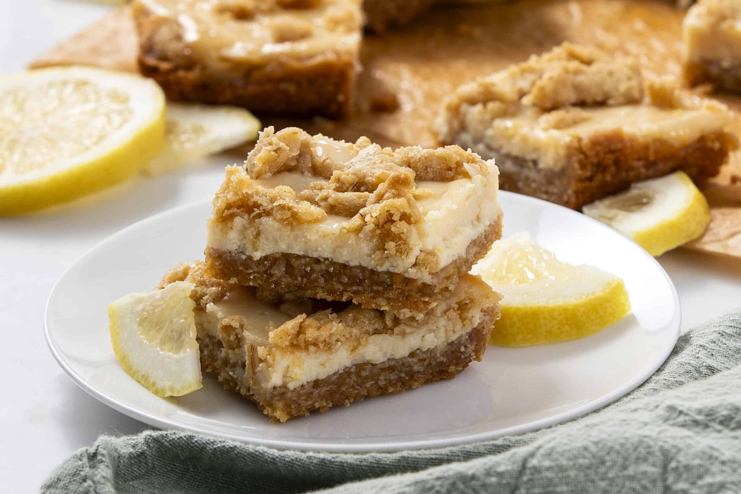 Delicious lemon dessert bars with a crumbly topping and creamy filling on a white plate, garnished with fresh lemon slices, perfect for spring or summer desserts.