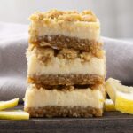 Sweet lemon bars with a crumbly crust and tangy lemon filling, stacked on a wooden board with lemon slices for garnish. Perfect for dessert or teatime treats.