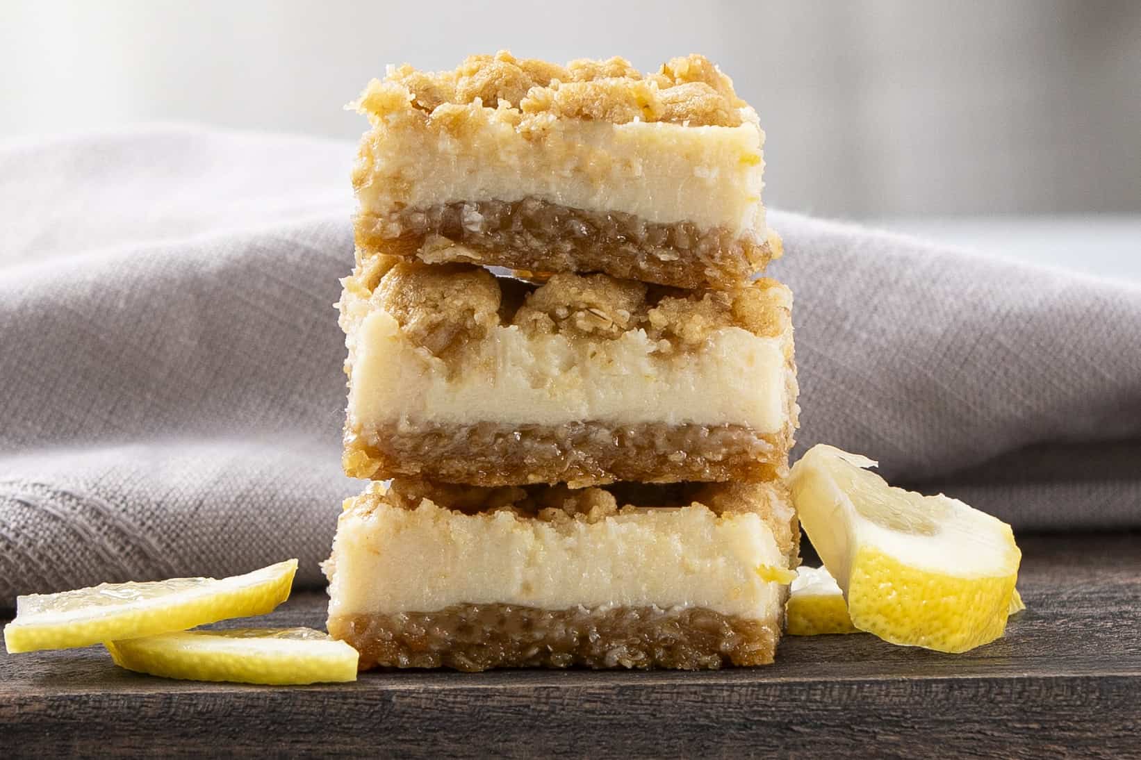 Sweet lemon bars with a crumbly crust and tangy lemon filling, stacked on a wooden board with lemon slices for garnish. Perfect for dessert or teatime treats.