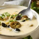 Creamy chicken and mushroom soup with black olives and fresh herbs in a rustic bowl, served with lemon and cilantro garnishes for a flavorful, comforting meal.