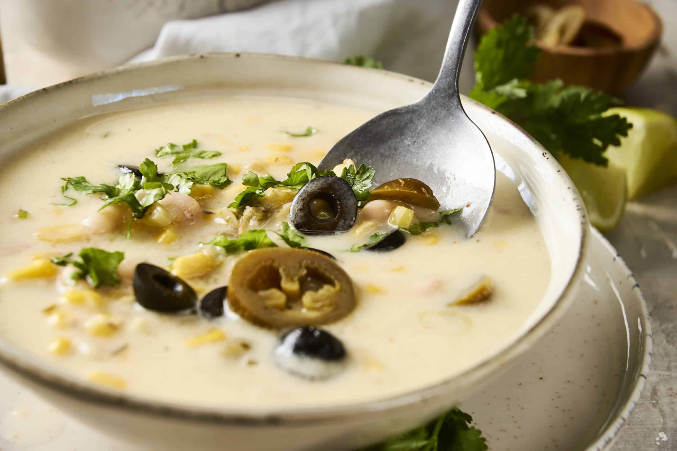 Creamy chicken and mushroom soup with black olives and fresh herbs in a rustic bowl, served with lemon and cilantro garnishes for a flavorful, comforting meal.