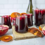 Vibrant homemade pomegranate and persimmon juice served in glasses with fresh fruit and ingredients on a rustic wooden board, perfect for healthy beverages and fruit recipes.