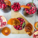 Juicy pomegranate and persimmon fruit drinks garnished with rosemary, served in glasses on wooden board with fresh fruits and striped cloth background, perfect for fall and winterrefreshing beverage.